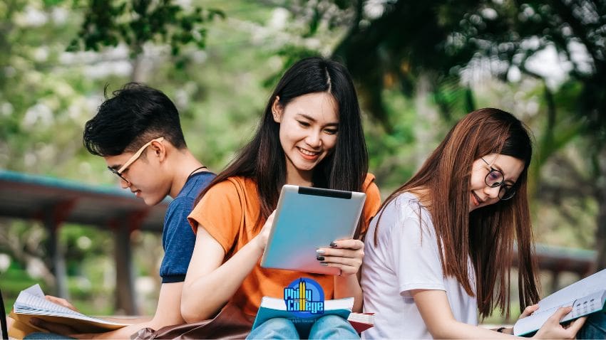 three students sitting on a bench and looking at a tablet