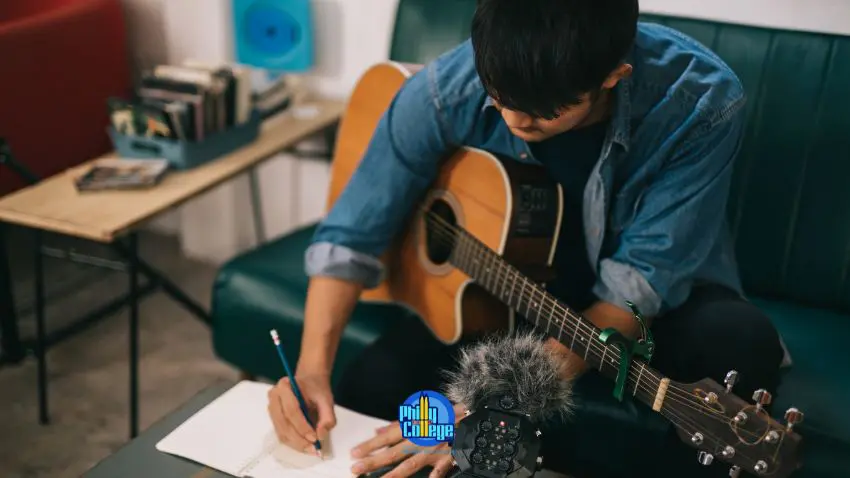 A person sitting on a couch with a guitar and notebook.