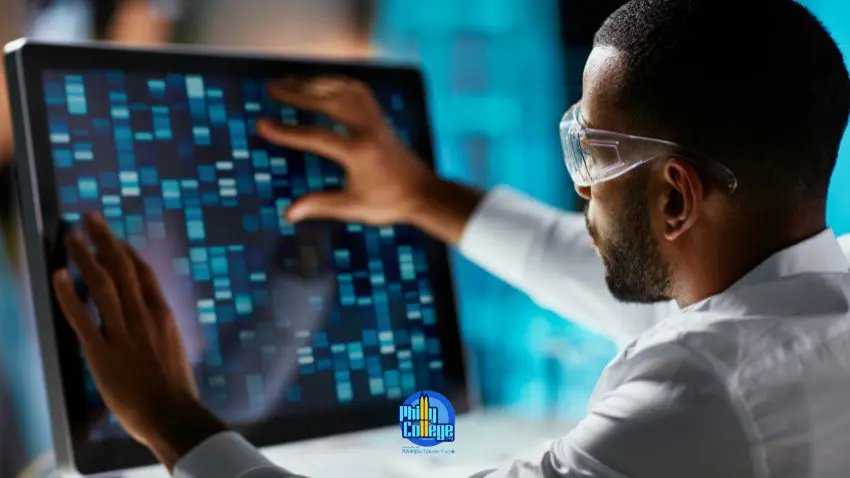 A person wearing safety glasses examines a computer screen displaying a grid of blue and white squares that resemble DNA sequencing data.