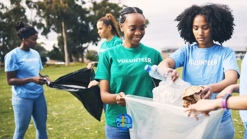 A group of volunteers in blue and green t-shirts are collecting trash in a park.