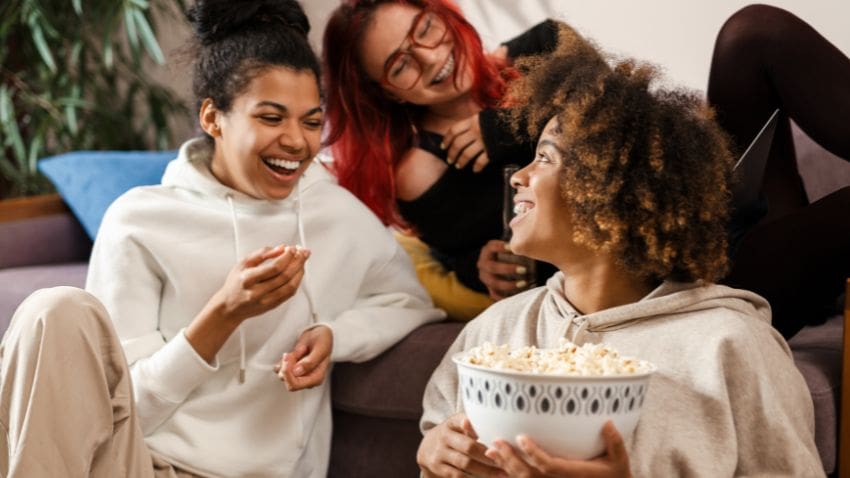 diverse group of woman laughing and eating pop corn on the couch