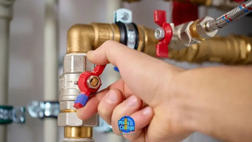A hand is turning a red and blue handle on a brass pipe fitting.