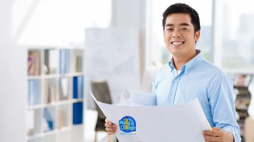 A man in a blue shirt holds blueprints and smiles at the camera in an office setting.