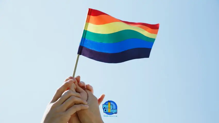two hands holding a rainbow flag in front of a blue sky