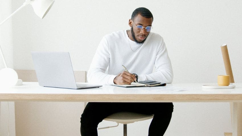 student at desk looking through paper work in front of laptop