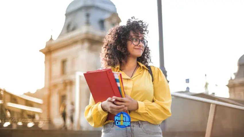 A person with glasses and a yellow shirt is holding a book.